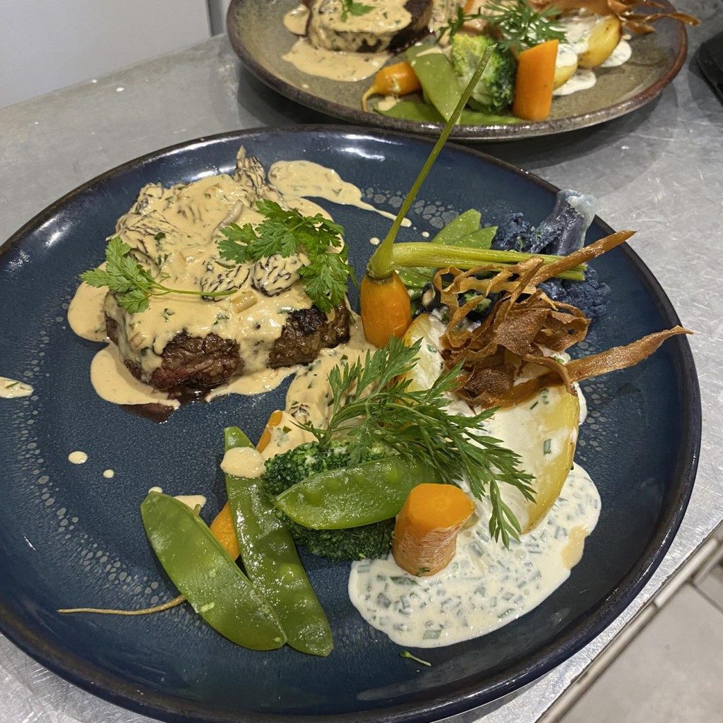 Une assiette creuse noire garnie de légumes, de viande et d'une sauce crémeuse
